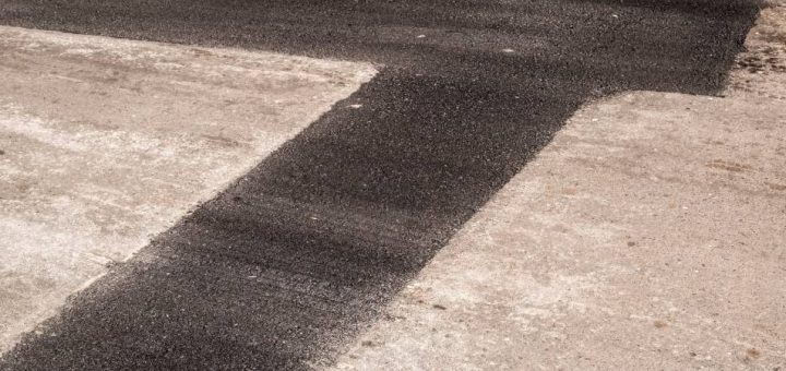 A recently repaired patch of road. There is a clear visible contrast between the fresh black new asphalt and the faded and cracked old road.