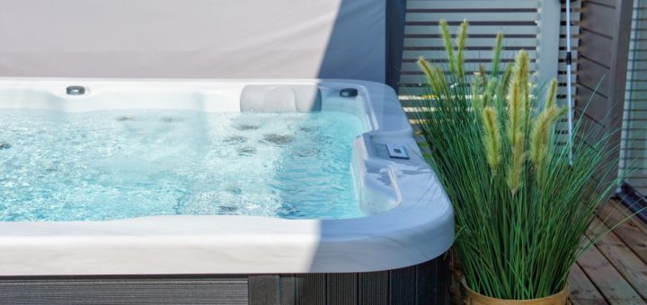 A close-up of a swim spa situated on a backyard patio. Next to the swim spa is a woven basket full of decorative grass.