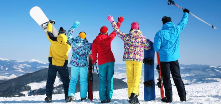 Five people stand with their backs turned on top of a snow-covered mountain wearing cold weather gear and skis.