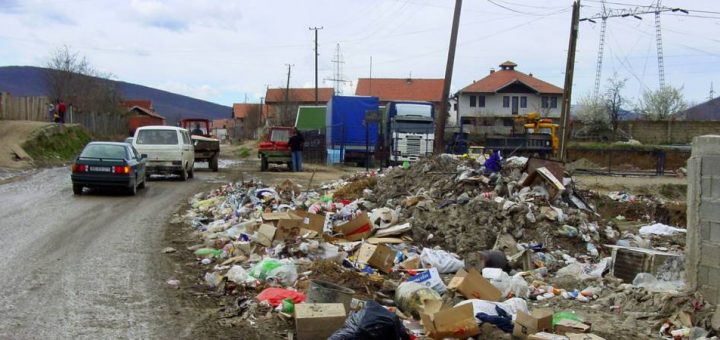 A small community in the wake of a disaster. There is rubble and debris everywhere, stacked along the roadway.