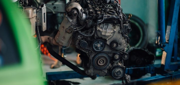 A dirty, worn-out automotive engine is being held up in a garage by metal chains and a chain lift.