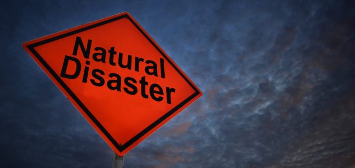An orange and black natural disaster sign outside on a dark, stormy day with a cloudy sky.