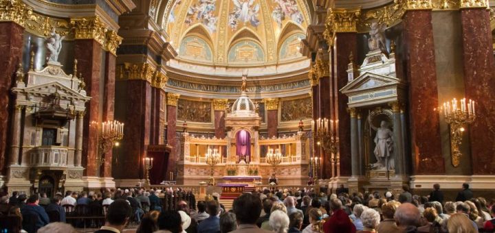 People fill the pews in St. Stephen's Basilica. The ornate architecture features marble, gold, and other premium materials.