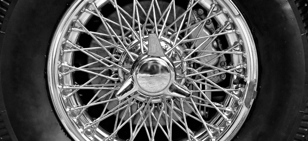 Close-up to a black tire using a chromed finish wire wheel with multiple interlaced wires and a large knob in the middle.