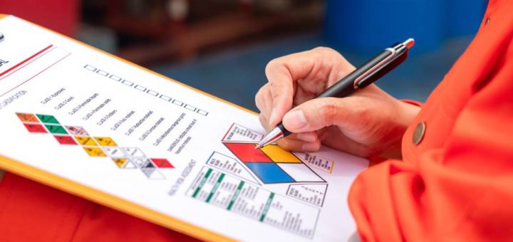 Close-up image of a safety inspector holding a clipboard with a sheet denoting various hazmat symbols and checkboxes.