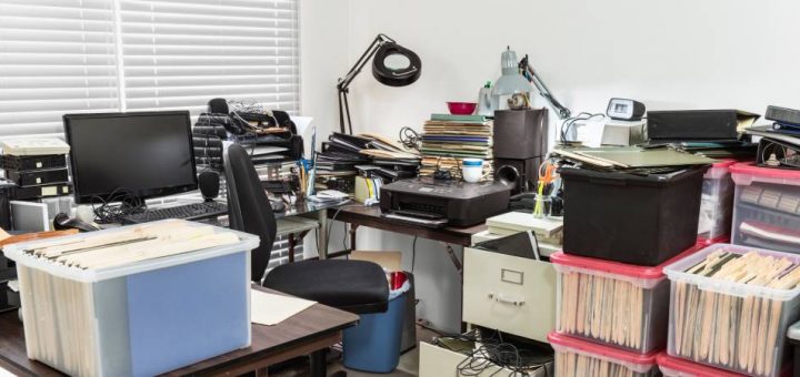 A messy workspace with clutter and disorderliness everywhere. The office appears to be very cramped and inefficient.