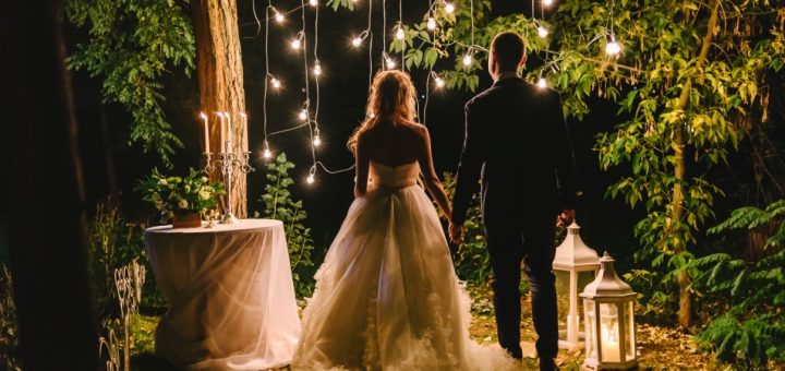 A bride and groom standing outside at night. They are standing in front of string lights hanging from a tree.
