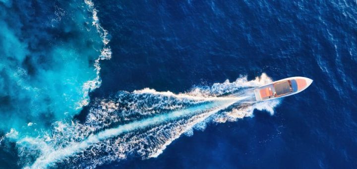 An overhead view of a boat on the ocean with wake behind it over the dark blue water during the daytime.