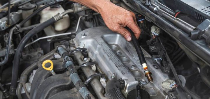 A close-up of a person working on a car engine and checking the spark plugs along with nearby components.