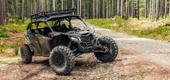 A black UTV with camouflage panels on the doors sits on a dirt and rock path surrounded by trees.