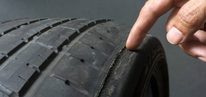 A close-up of a finger pointing to damage on a tire's tread. The tire is old and worn down on the sides.