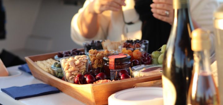 A woman standing over a charcuterie board on a boat. The board has various foods like cherries, almonds, and grapes.
