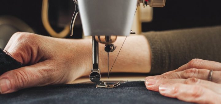A close-up view of a woman’s hands working with fabric and a sewing machine to stitch a denim craft.