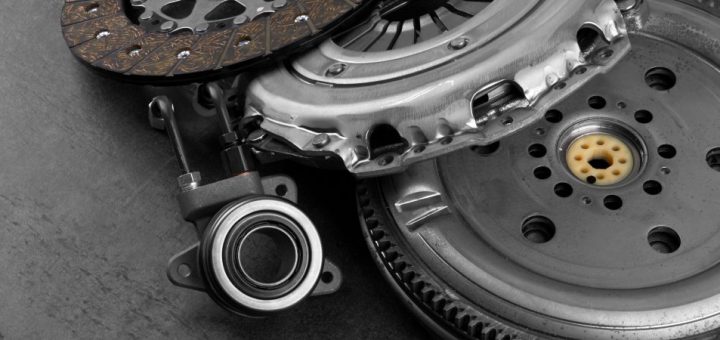 A close-up of an automotive clutch kit, including the clutch disc and clutch release bearing, on a grey table.