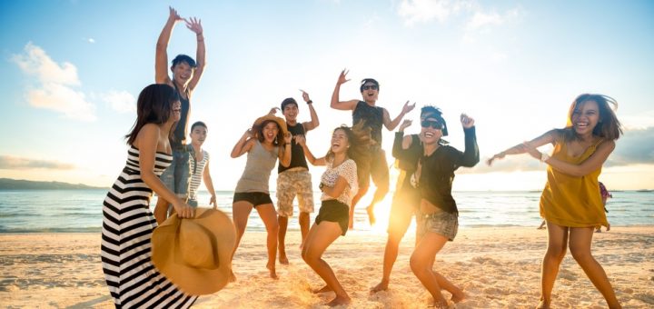 A group of friends are on the beach and having fun dancing with each other while the sun sets behind them.
