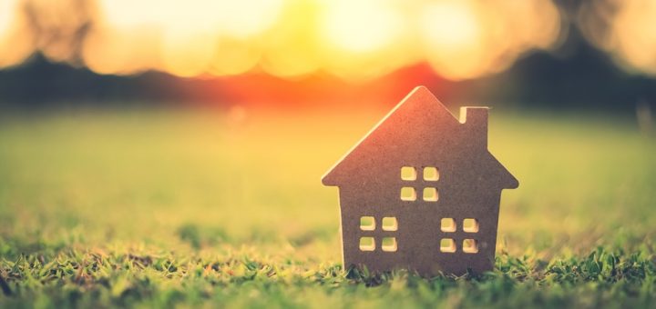 A small model of a house sits on a neatly trimmed lawn. It is the golden hour, and the sun illuminates the grass.