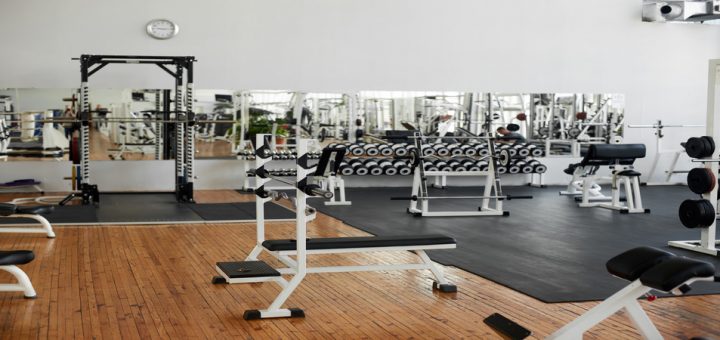 A commercial gym contains various gym equipment, including a weight rack, a bench press, and a squat machine.