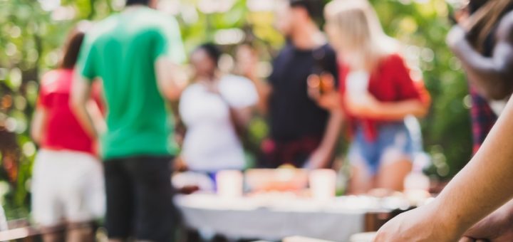 A group of friends gathered around a picnic table. The grill is up close and there are skewers being cooked.