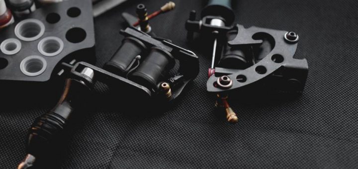 Tattoo supplies, including a tattoo machine, ink bottles, and a black holder with ink containers, rest on a black surface.
