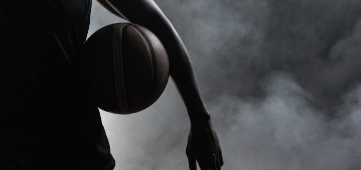 The silhouette of a man against a smoky background, standing with a basketball hugged to his side with his arm.