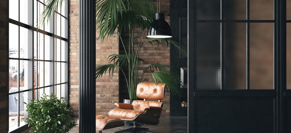 A living room loft featuring brick walls, a mid-century modern armchair, and industrial-style black finishes.