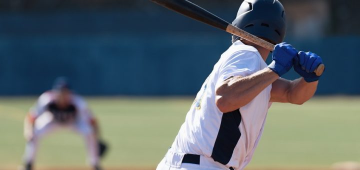 A batter anticipating a pitch as they hold onto a black wooden bat. They're wearing a black helmet in a white uniform.