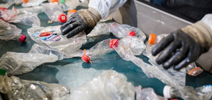 A worker wearing protective waste gear is working on a factory line while sorting through plastic waste.