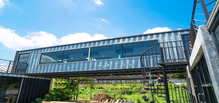 Several desks inside a metal shipping container raised above the ground with greenery in the background.