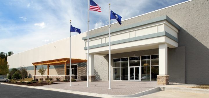 Three separate flags flying atop flagpoles at different heights outside a white-colored commercial building.