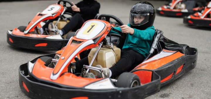 A young child driving a go-kart with a number 1 on the front. An older man is driving a go-kart behind him.