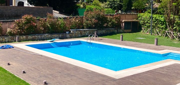 A rectangular backyard swimming pool with a diving board surrounded by a wood deck and mature landscaping.