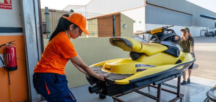 Two workers collaborating to move a black-and-yellow personal watercraft into a garage space.