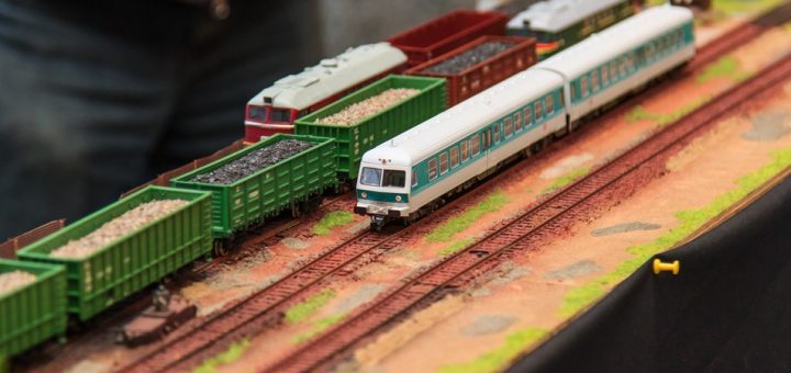 A table features a model train scene with green and white trains, a red and white train, and mossy areas.