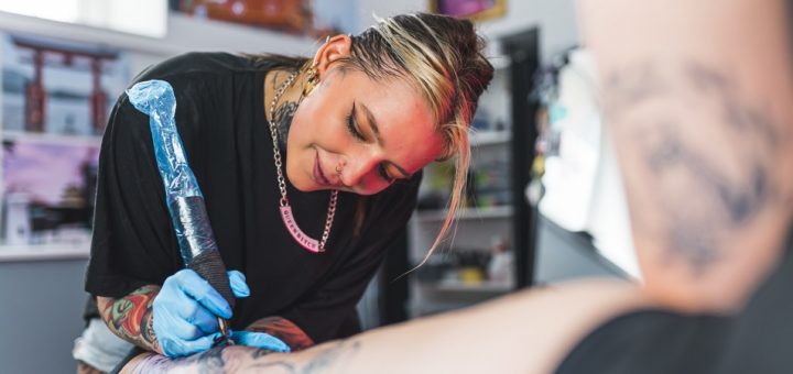 A close-up of a happy professional female tattoo artist makes a tattoo in the studio on a client's leg.