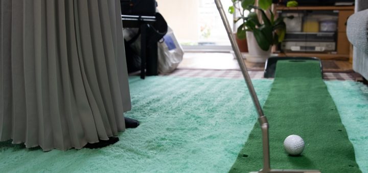 A woman practices her golf putts at home, hitting balls on a mat that looks like a golf green and leads to a hole.