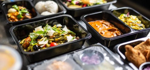Several open and closed black plastic takeout containers filled with different types of colorful food.