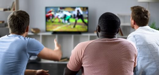Rear view of three men, watching sports together on a TV screen. One holds up his hand in frustration.