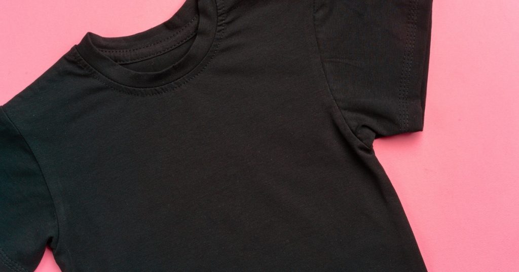 A plain, black t-shirt that's clean and free of wrinkles, laid flat against a bubblegum pink background.