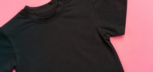 A plain, black t-shirt that's clean and free of wrinkles, laid flat against a bubblegum pink background.