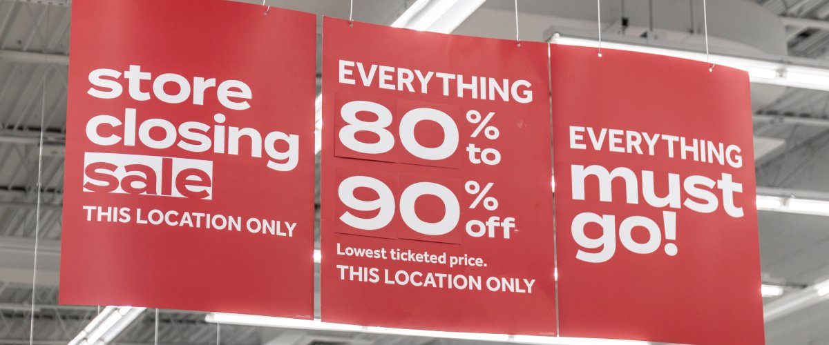 Red marketing banners inside a business hanging from the ceiling. The banners have white lettering for a sale.