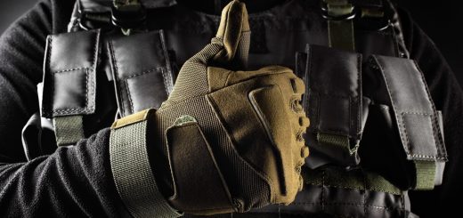 A close-up of a person wearing military-grade tactical gear, such as a bulletproof vest and safety gloves, with a thumbs-up.