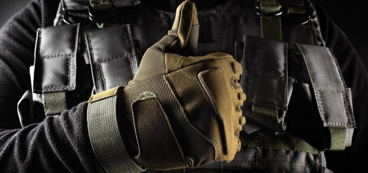 A close-up of a person wearing military-grade tactical gear, such as a bulletproof vest and safety gloves, with a thumbs-up.