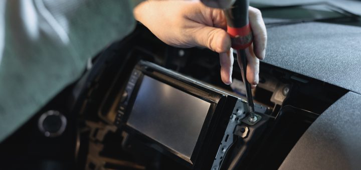 Someone installing a new car radio. They are holding a screwdriver in one of the screws next to the radio.