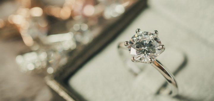 A gold ring with a large diamond incrusted on top, clipped to the interior of a beige box with a blurry background.