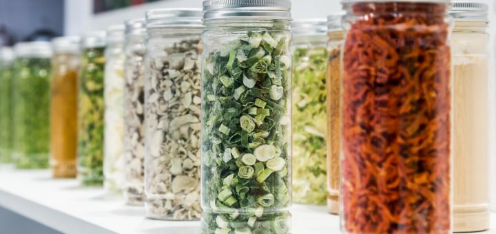 A group of colorful freeze-dried vegetables and fruits sliced and ground in glass jars in a shop window.