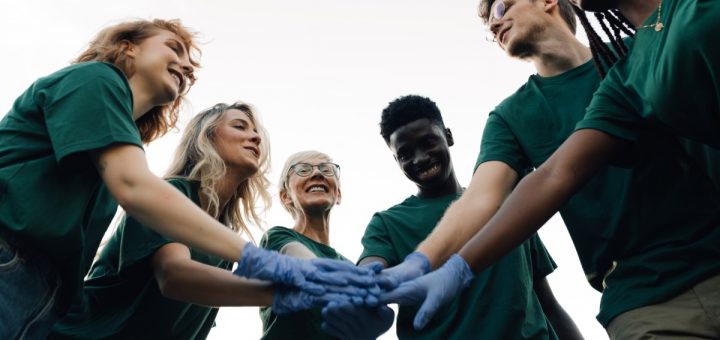 A diverse group of happy volunteers, laughing and joining hands while wearing gloves before volunteering.