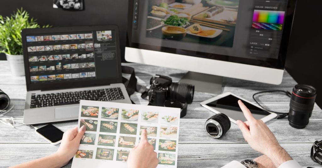 Two sets of hands both pointing at photographs. There is also a computer screen with editing software on it.