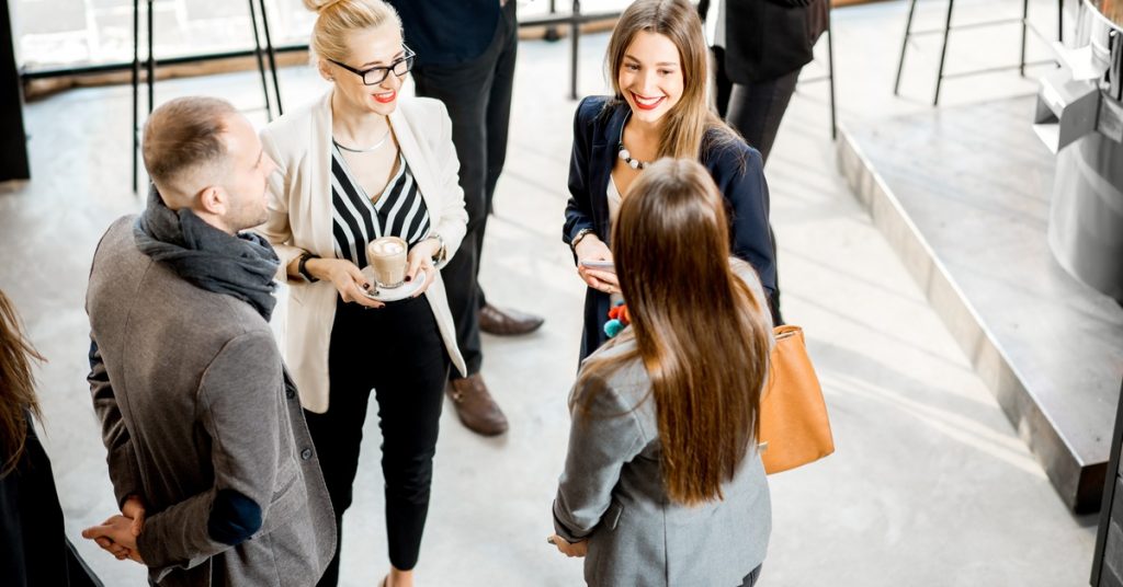 A group of four well-dressed businesspeople standing in a circle at a corporate event talking to one another.
