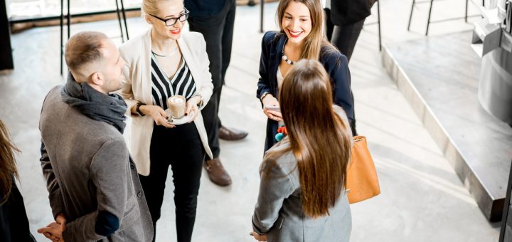 A group of four well-dressed businesspeople standing in a circle at a corporate event talking to one another.