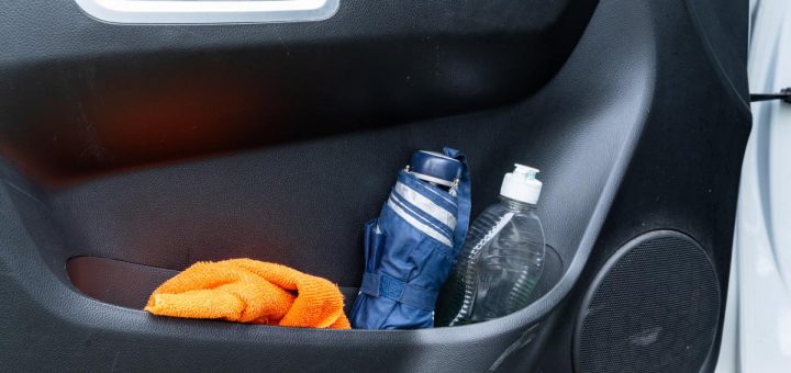 A close-up of the inside of a vehicle's door. The door pocket has a cloth, an umbrella, and a bottle of soap.